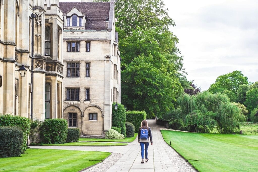 Bachelor's degree student walking down sidewalk beside a large stone academic building. What is a Bachelor's Degree: A Guide to College Majors