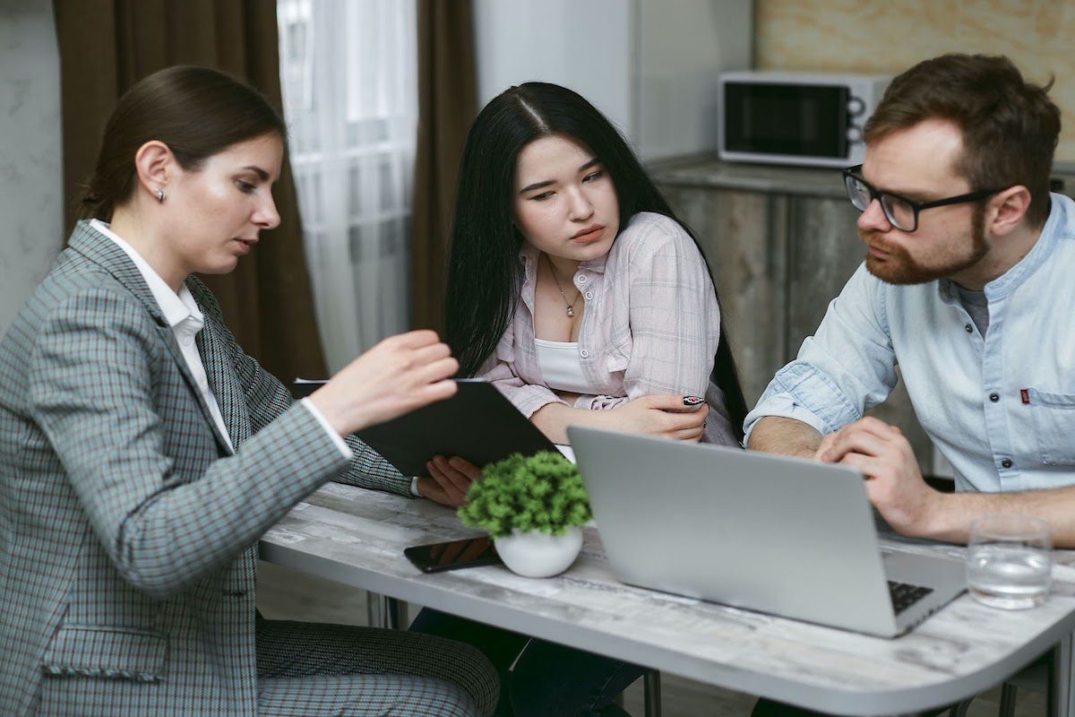 Three people discussing around a table with a laptop on it