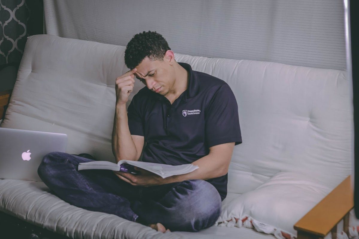 A man studying with a book and laptop while sitting on a couch. Best Online Mechanical Engineering Bachelor's Degrees