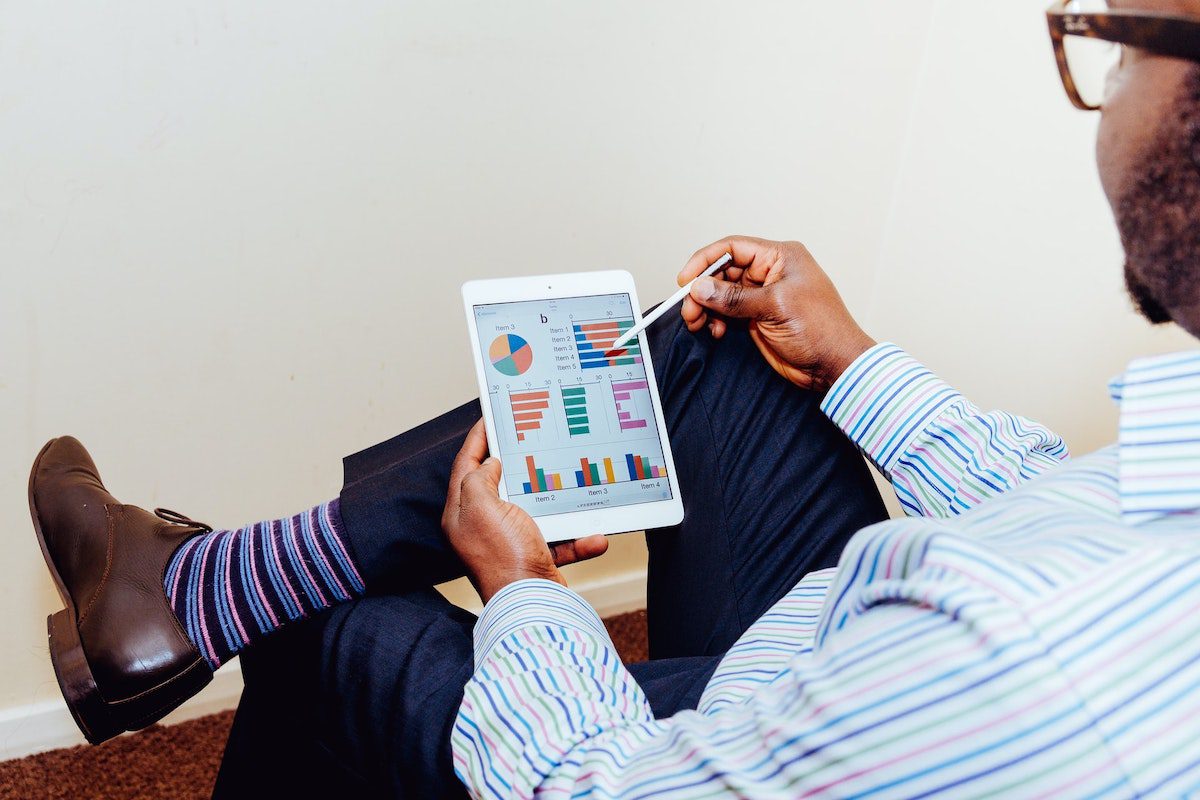 Man in a striped shirt sitting down looking at graphs on an iPad mini